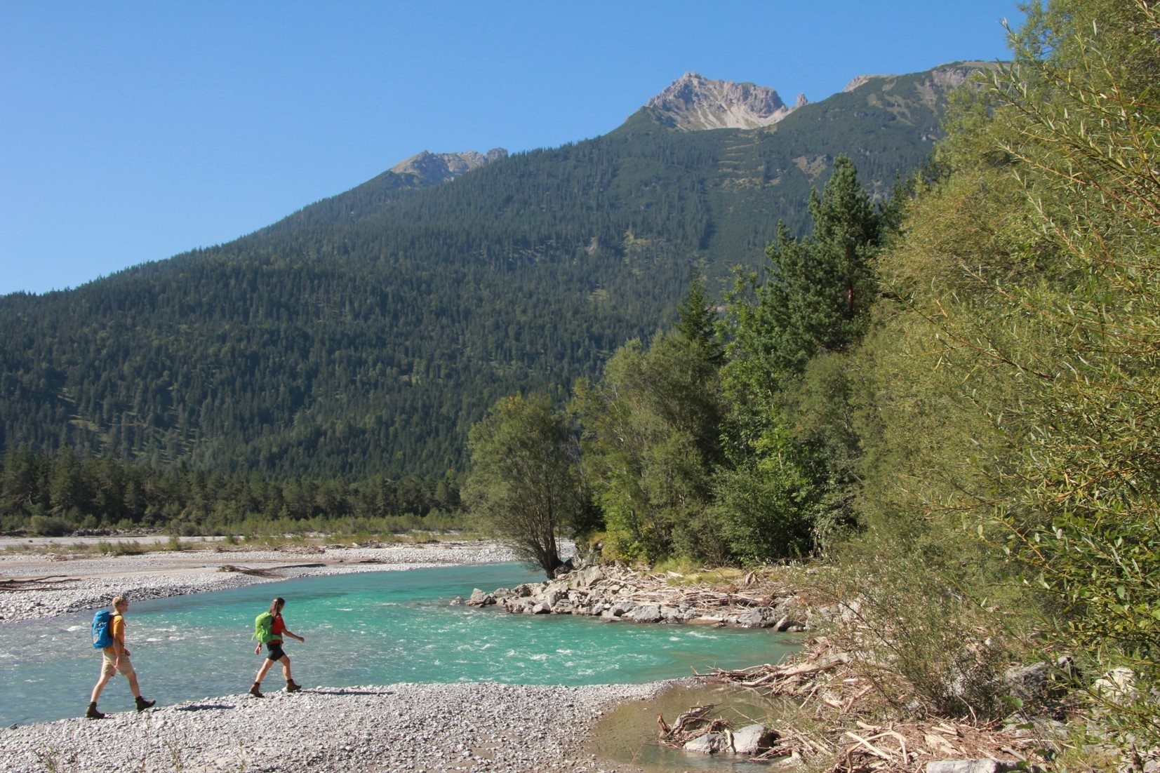 Wanderweg über eine Wiese im Lechtal bei Forchach, dahinter das Flussbett des Lech und bewaldete Berghänge